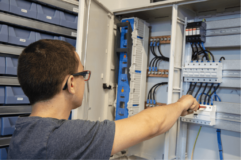 Technician operating an electrical control cabinet, adjusting a circuit breaker inside a wired distribution panel.
