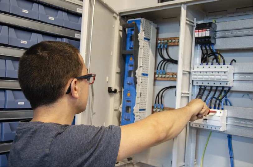 Technik w kamizelce serwisowej wykonuje prace przy instalacji elektrycznej na konstrukcji dachowej, pokazując elementy profesjonalnego montażu, jakiemu podlegają nowoczesne dachy z fotowoltaiką