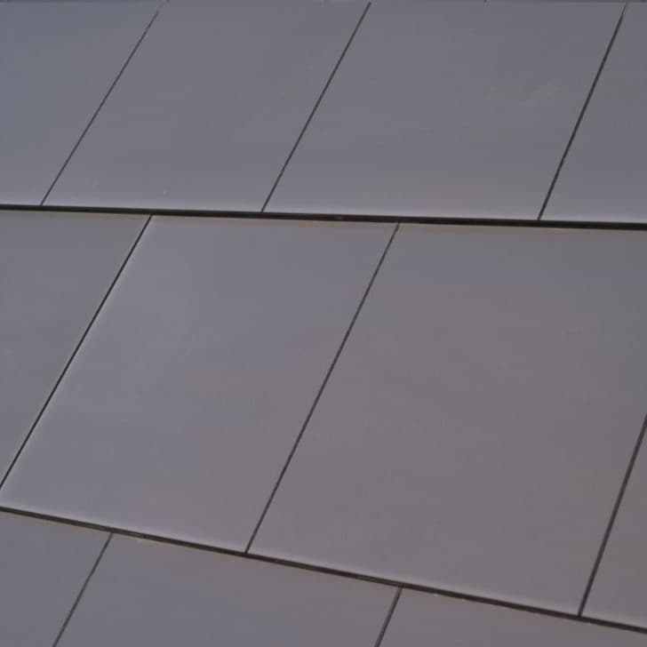 Zbliżenie na gładkie, grafitowe dachówki fotowoltaiczne ułożone w równych rzędach na połaci dachu