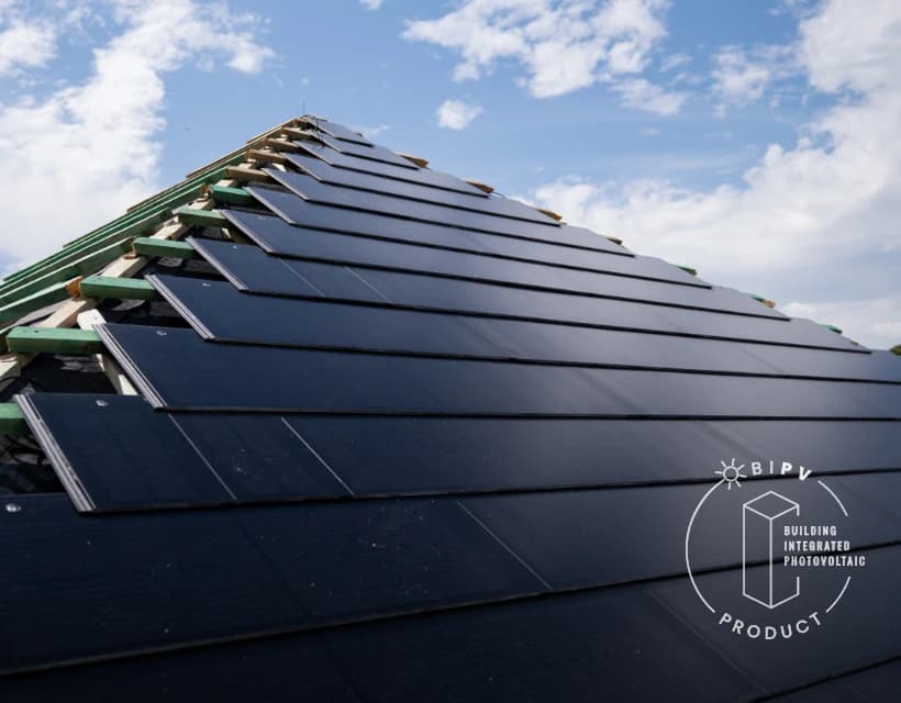 Close-up of a pitched roof during installation of black photovoltaic roof tiles (BIPV), rows aligned toward the ridge under a blue sky.