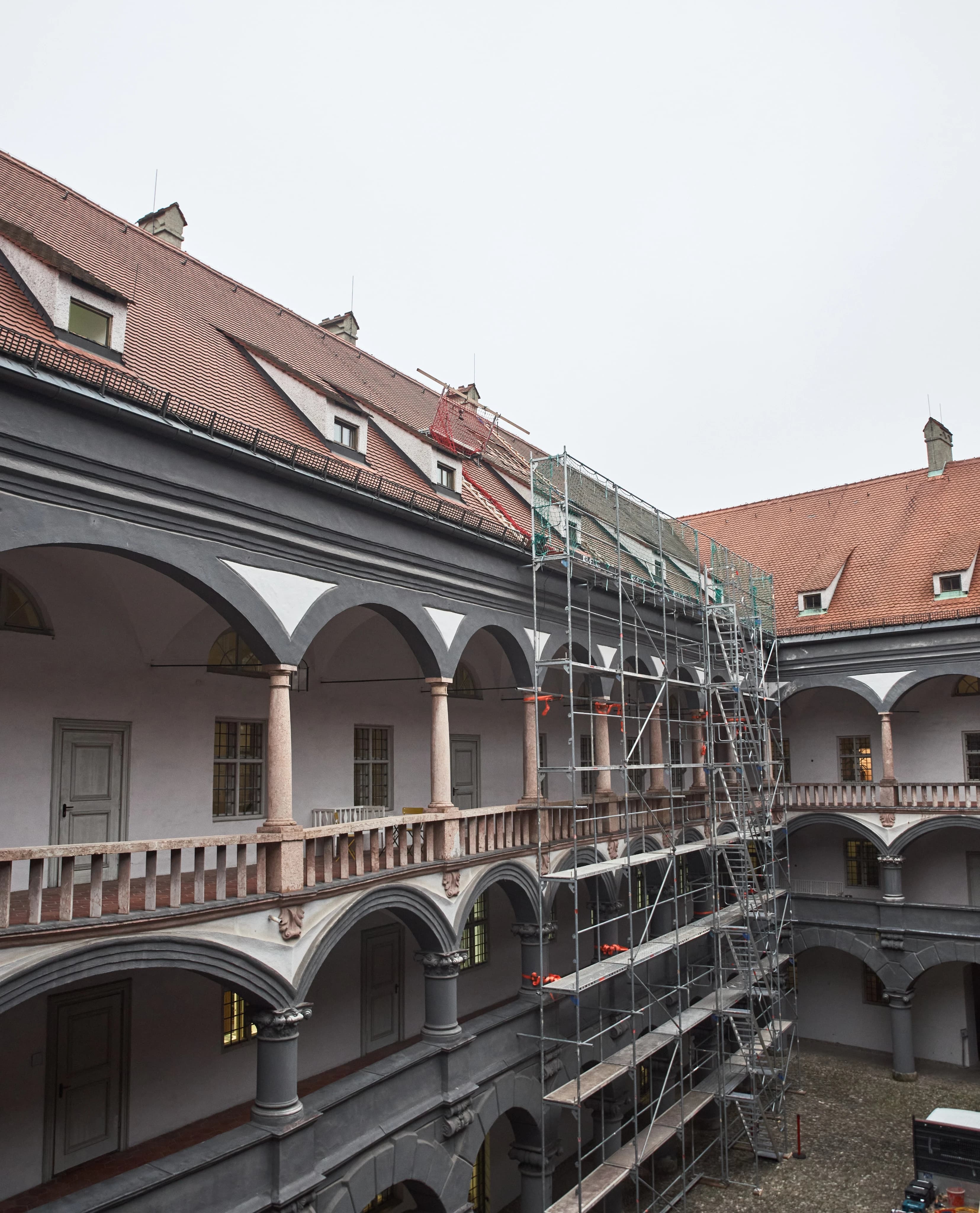 A wide shot of a historic courtyard. A section of the red-tiled roof is under renovation