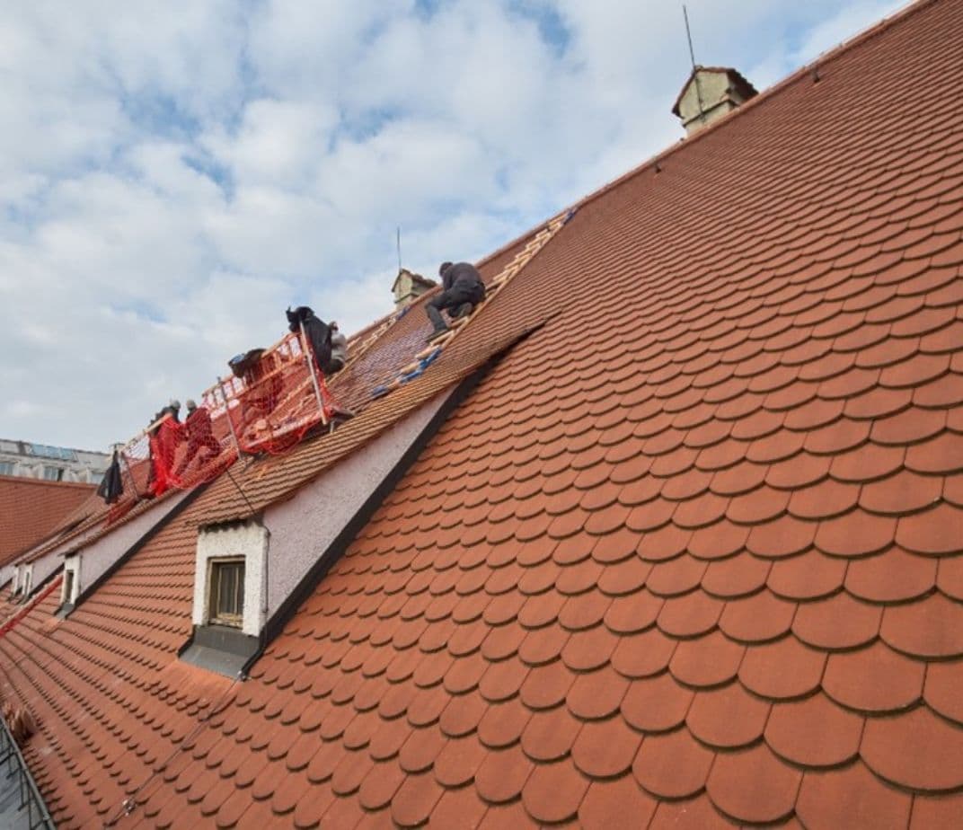 Workers are renovating a steep red-tiled roof on a historic building