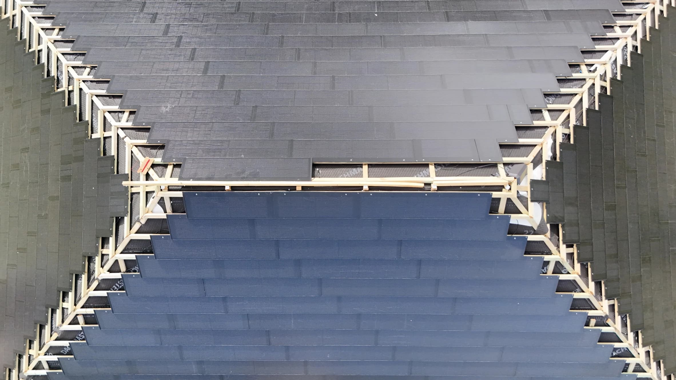 Close-up aerial view of a roof under construction showing dark solar tiles