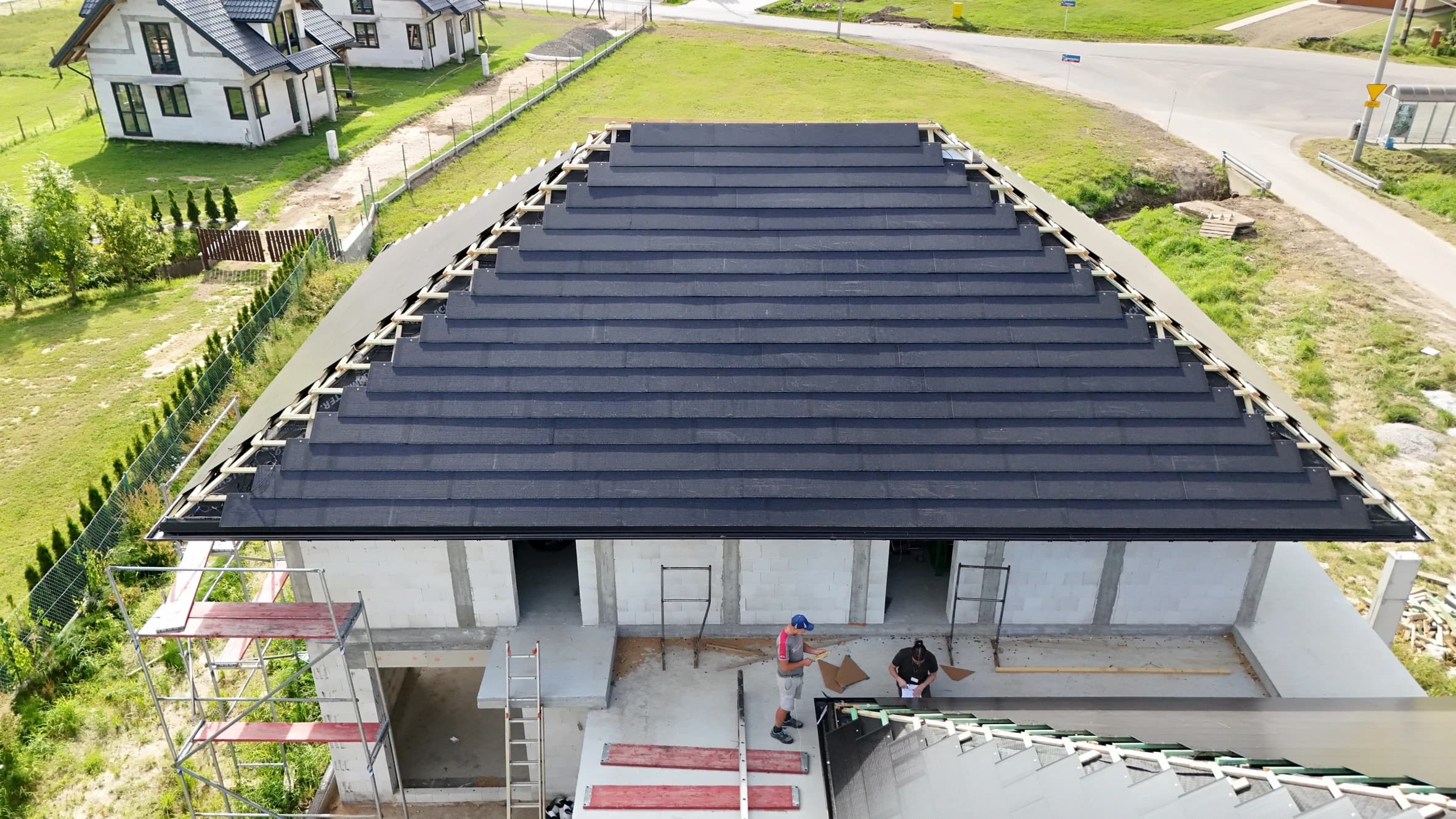 Aerial view of a modern house under construction with a dark solar or composite tile roof nearly completed