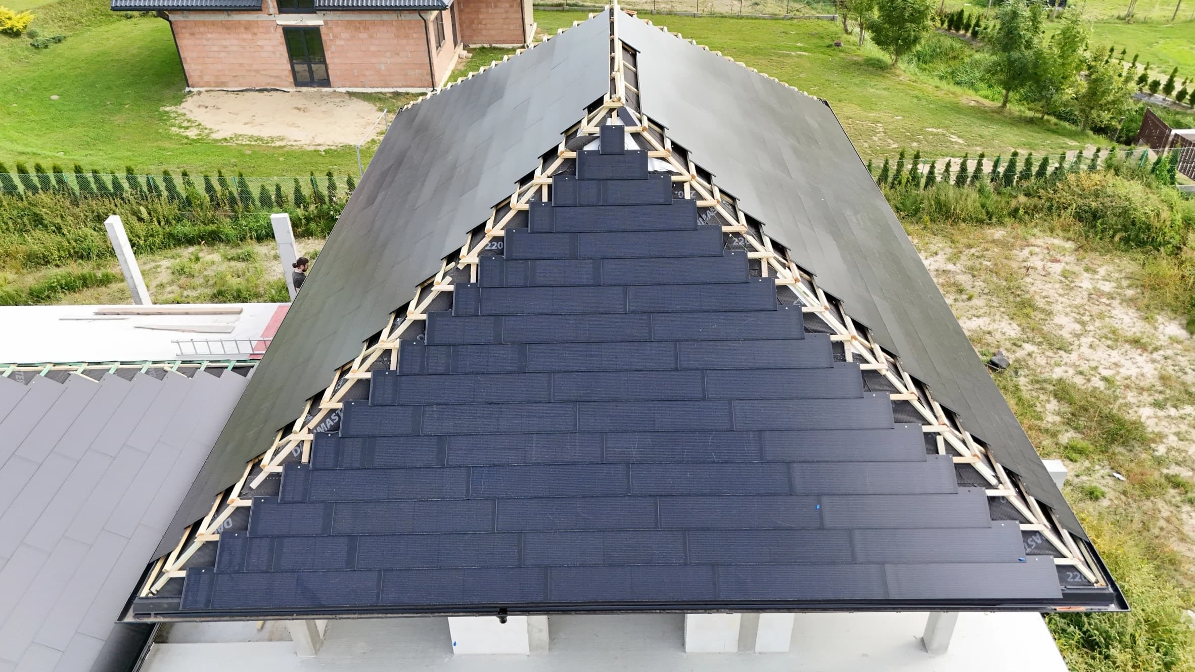 Aerial view of a modern house under construction featuring a dark, partially completed gable roof made of sleek solar photonroof tiles